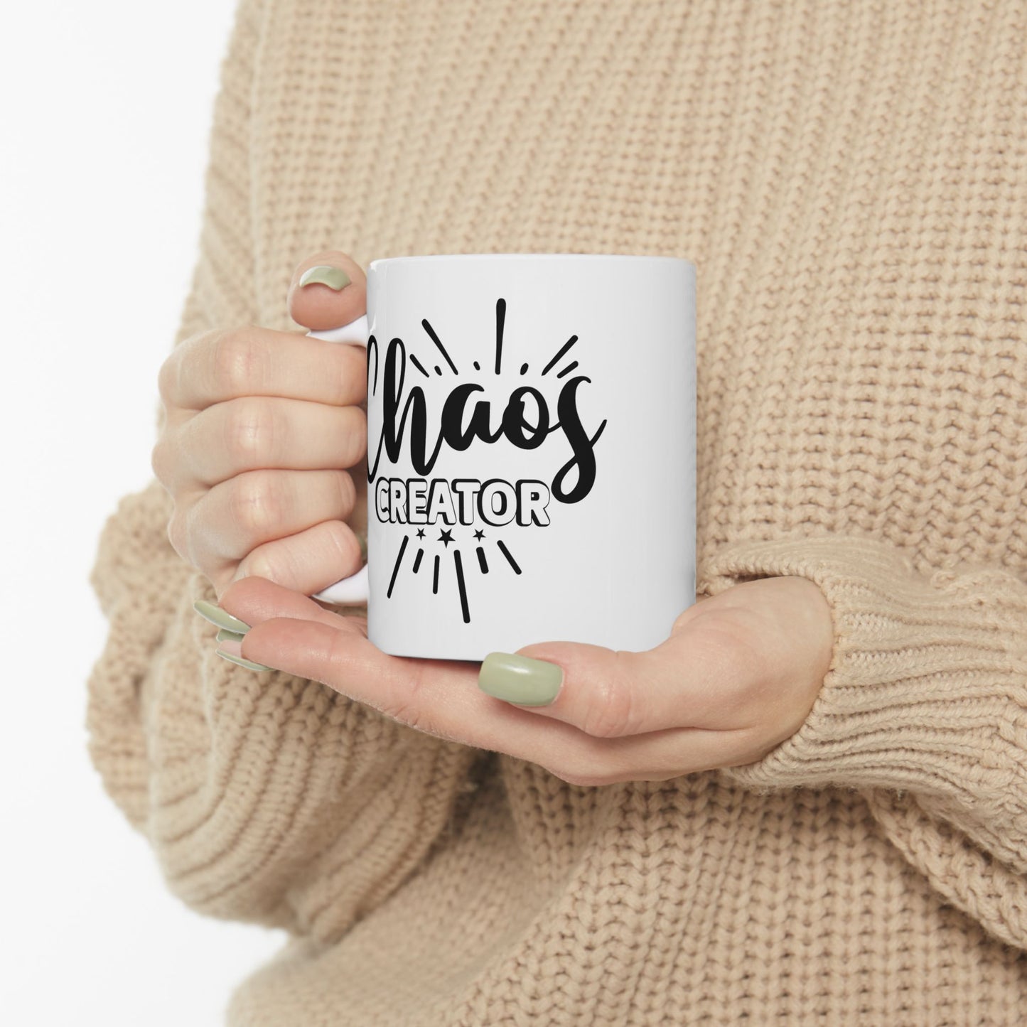 Person holding a white mug with 'Chaos Creator' text in black, wearing a beige sweater.