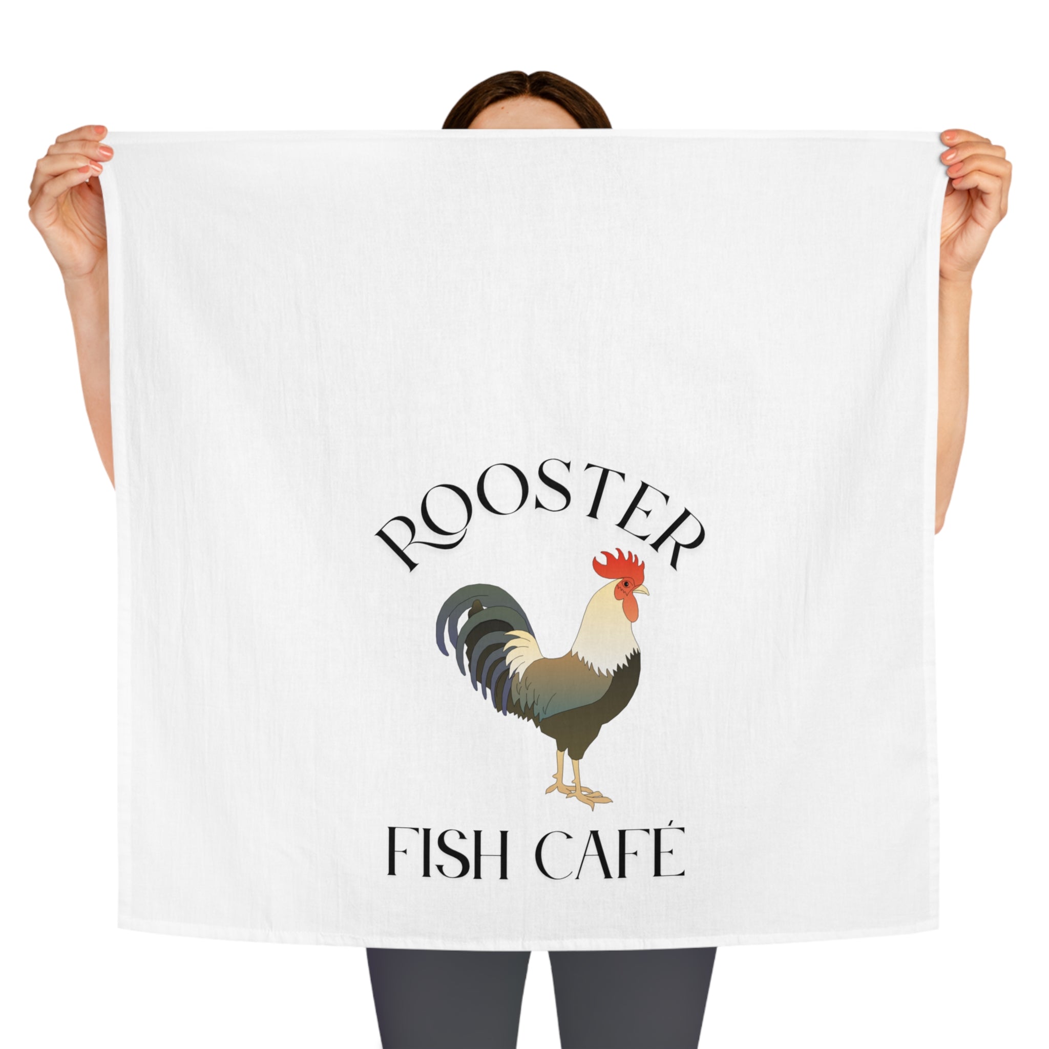 Person holding a white towel with a rooster design and 'Rooster Fish Cafe' text.