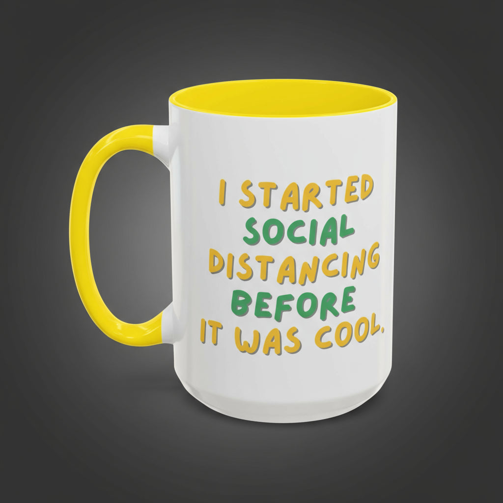 White mug with yellow handle and text 'I started social distancing before it was cool' on a white background