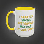 White mug with yellow handle and text 'I started social distancing before it was cool' on a white background
